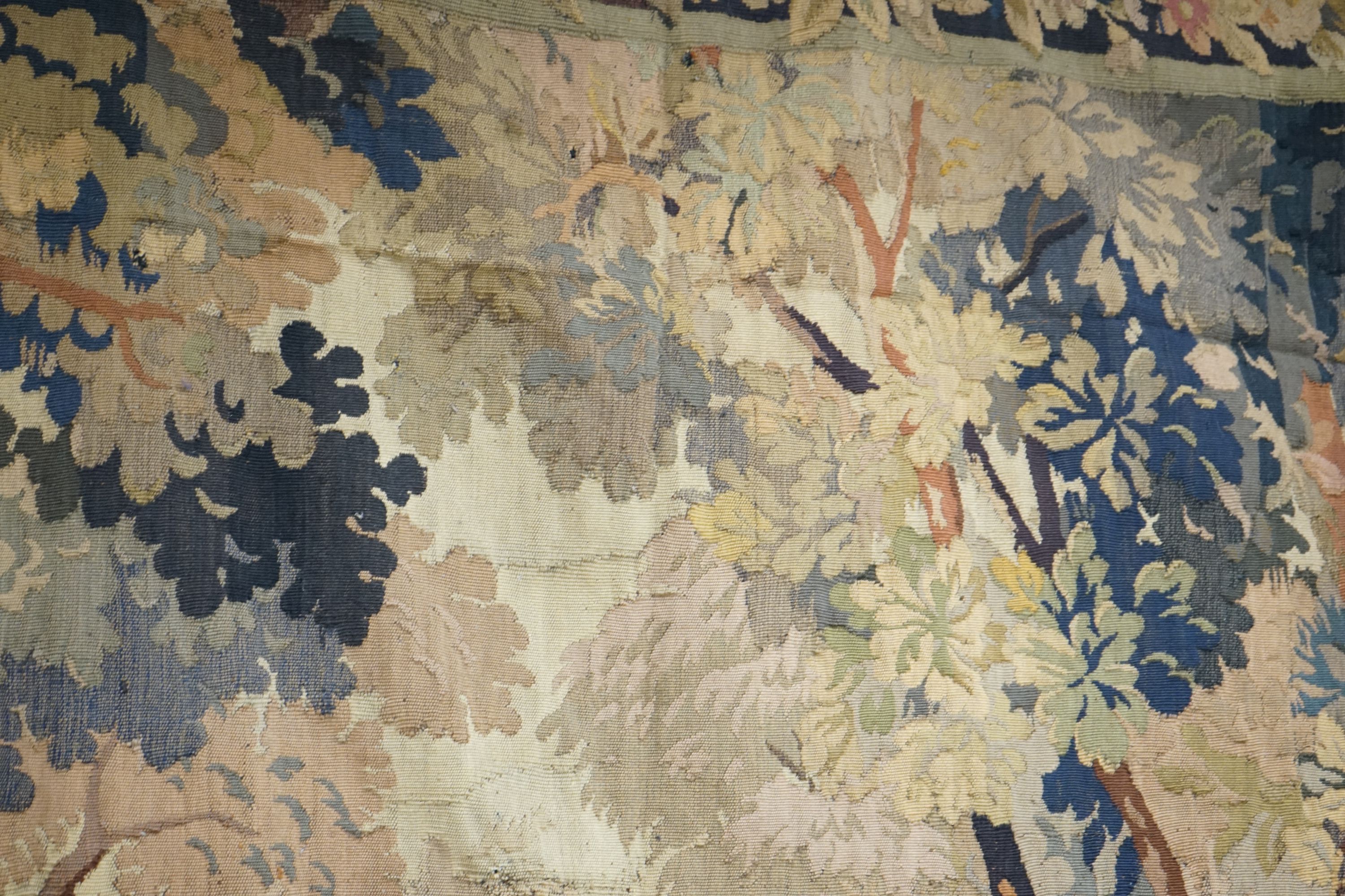 A late 19th / early 20th century French tapestry depicting a woodland scene with trees and flowers with a floral border woven in autumnal colours